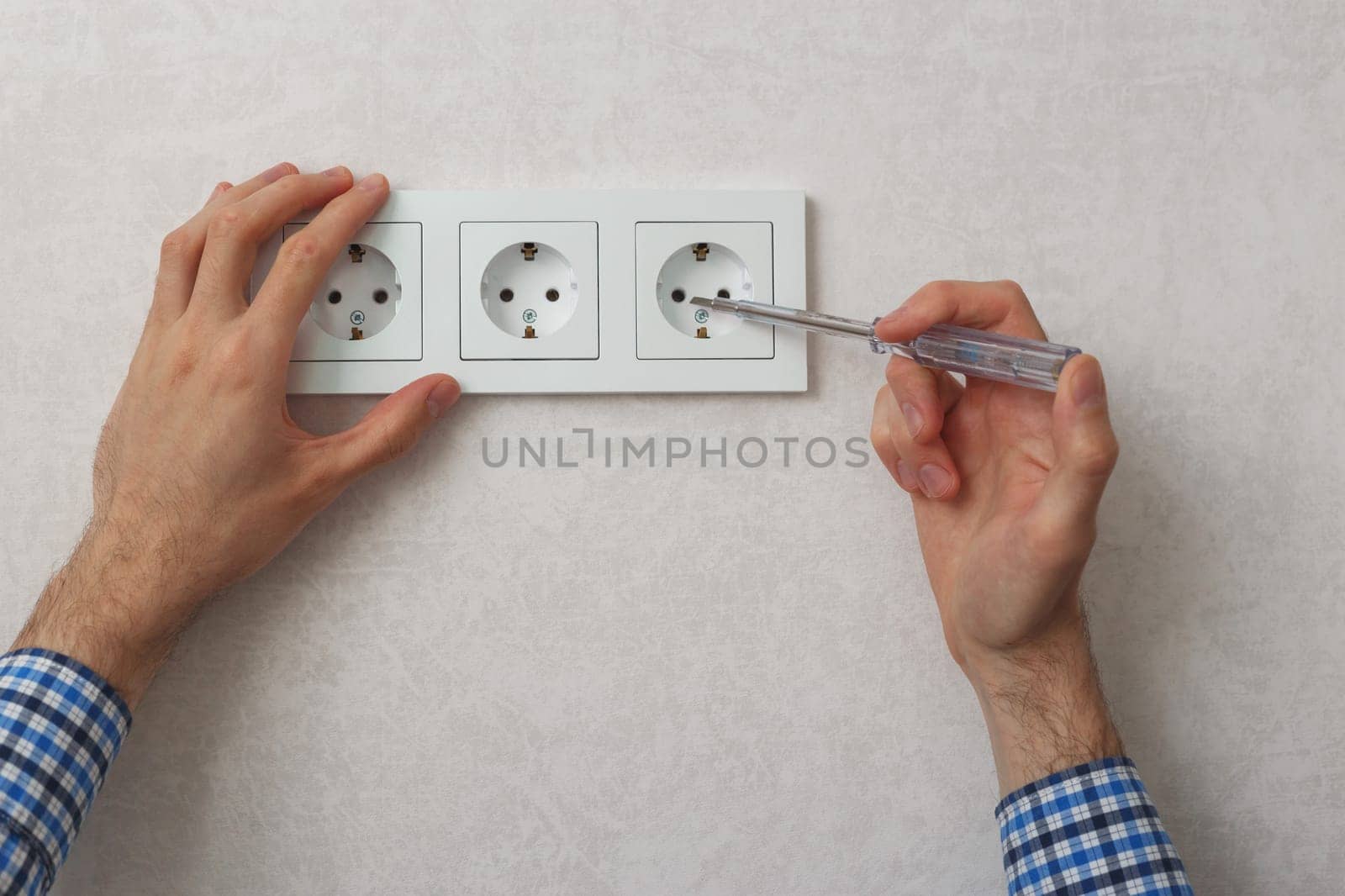Hand of electrician using phase tester screwdriver to repair wall socket.