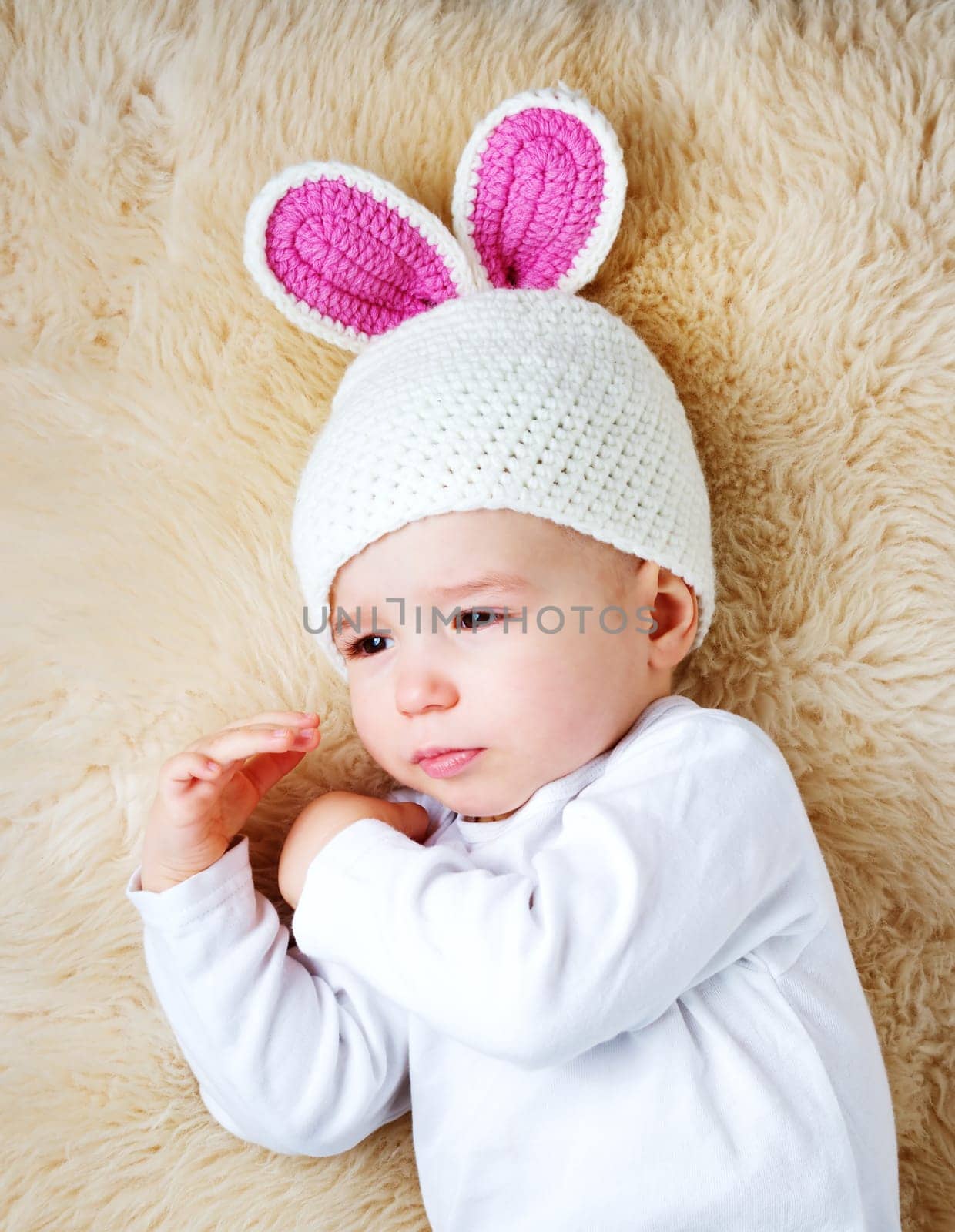 sleepy one year old baby lying in bunny hat on lamb wool background