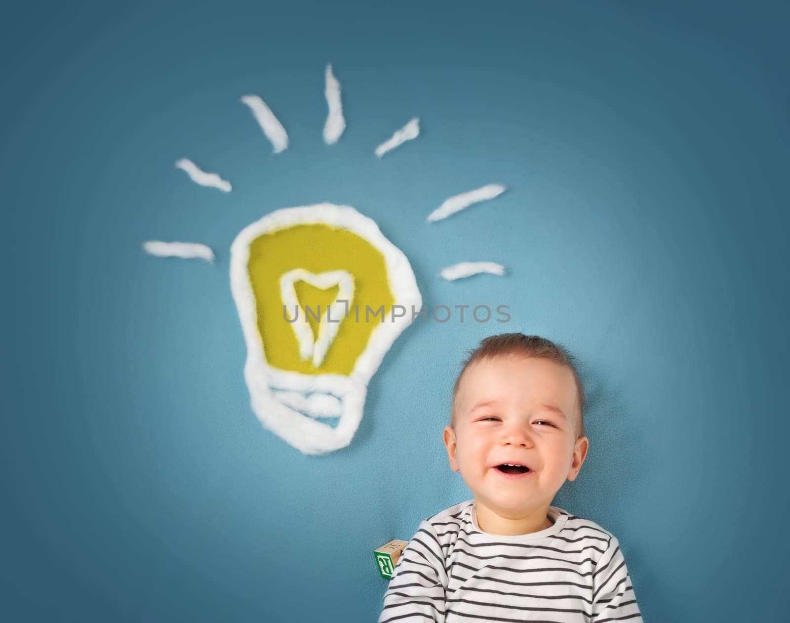 One year old boy with a bulb on blue background. Child with an idea