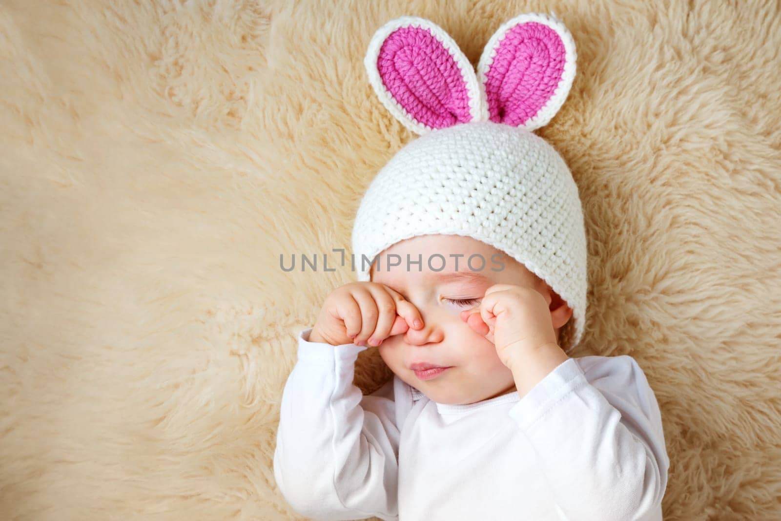 sleepy one year old baby lying in bunny hat on lamb wool background