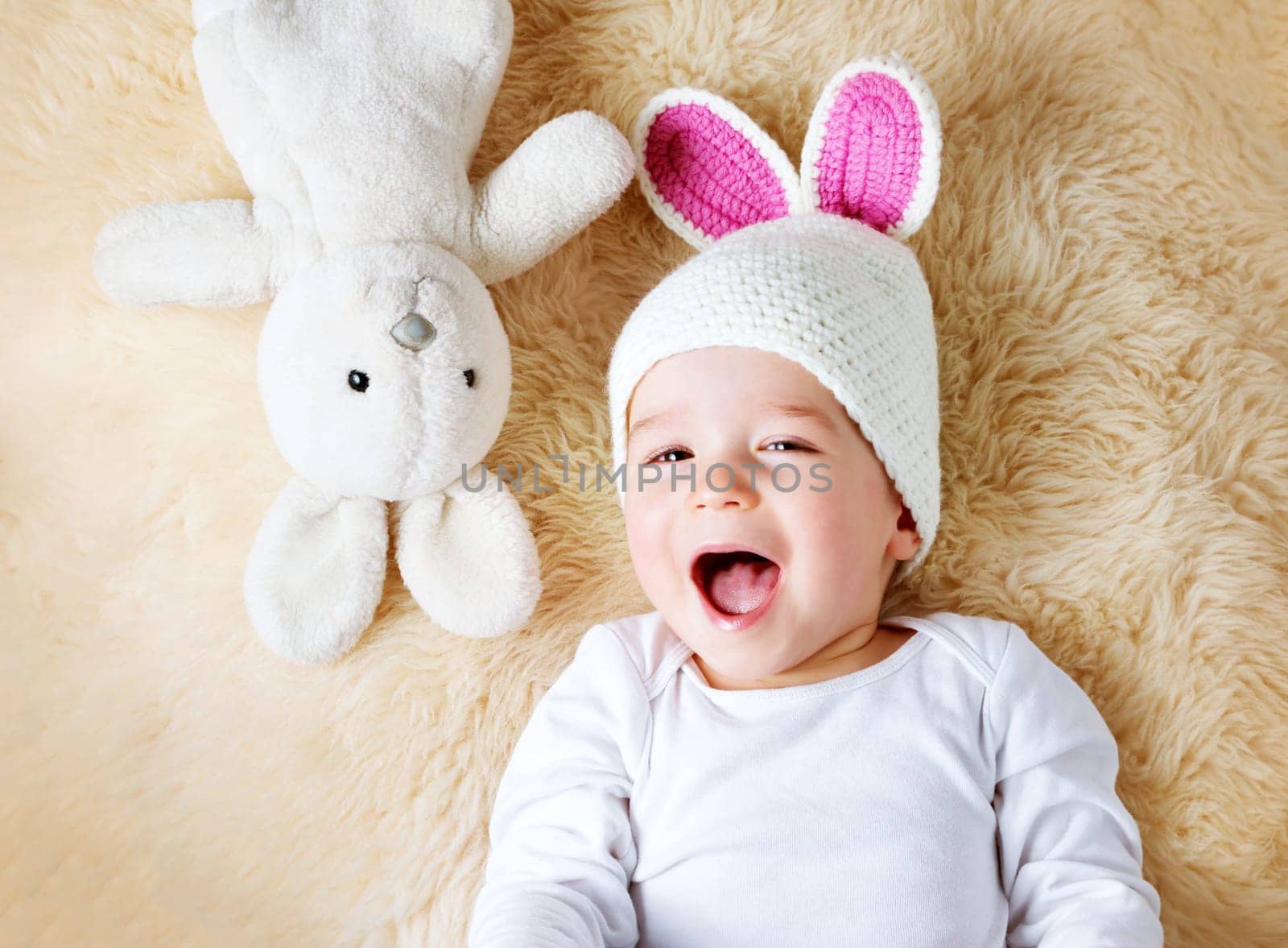 sleepy one year old baby lying in bunny hat on lamb wool background