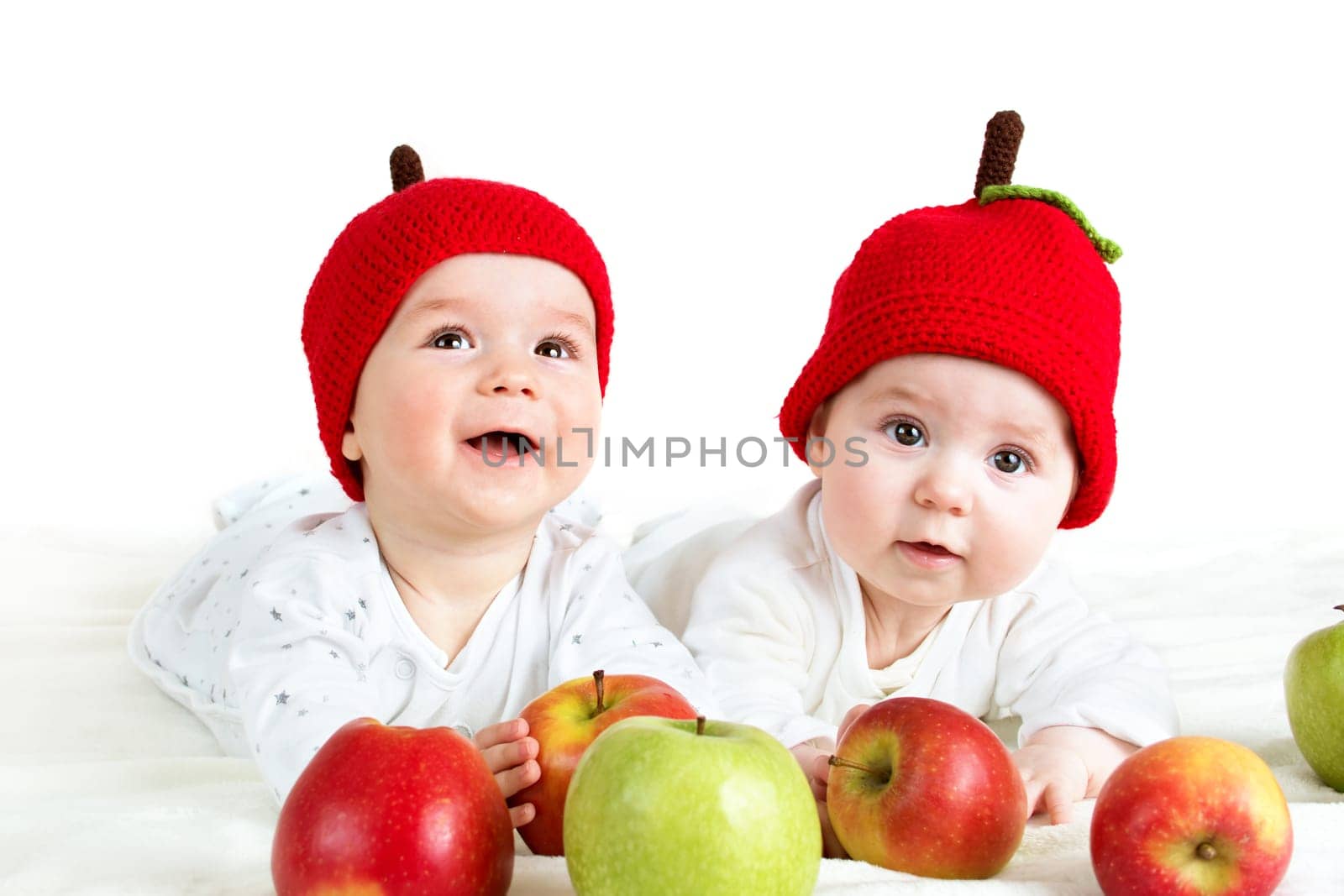 two cute six month old babies lying in hats on soft blanket with apples