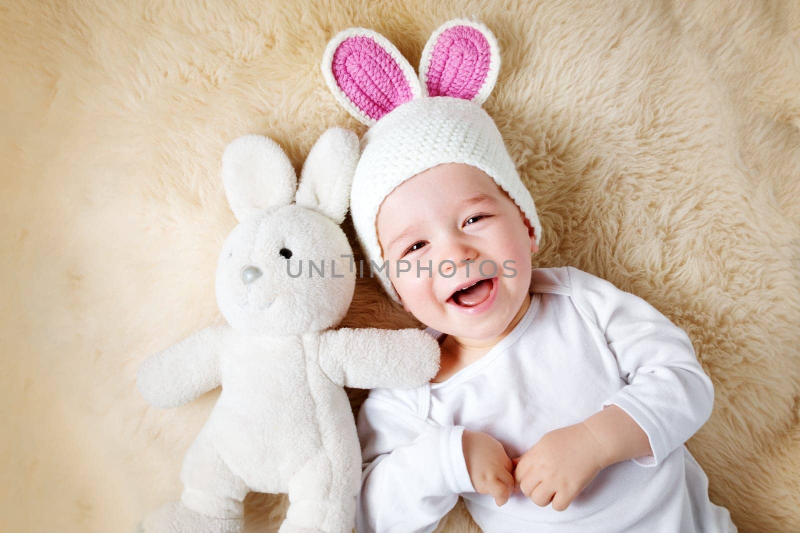 sleepy one year old baby lying in bunny hat on lamb wool background