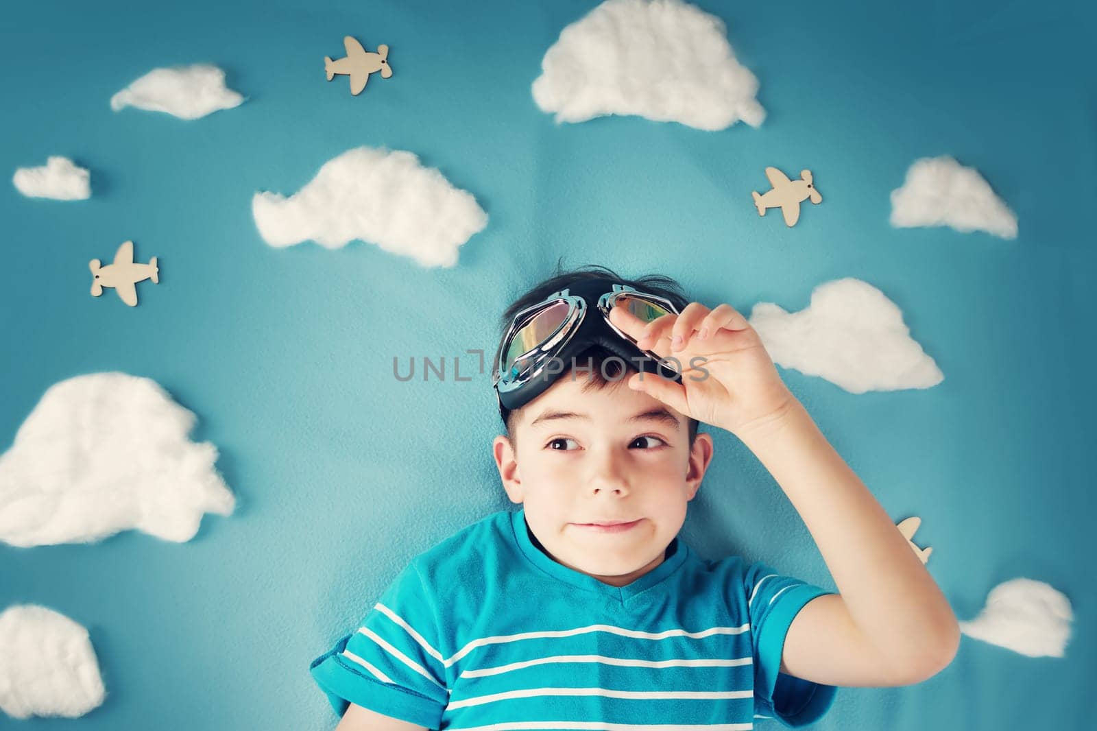 boy lying on blanket with white clouds in pilot glasses