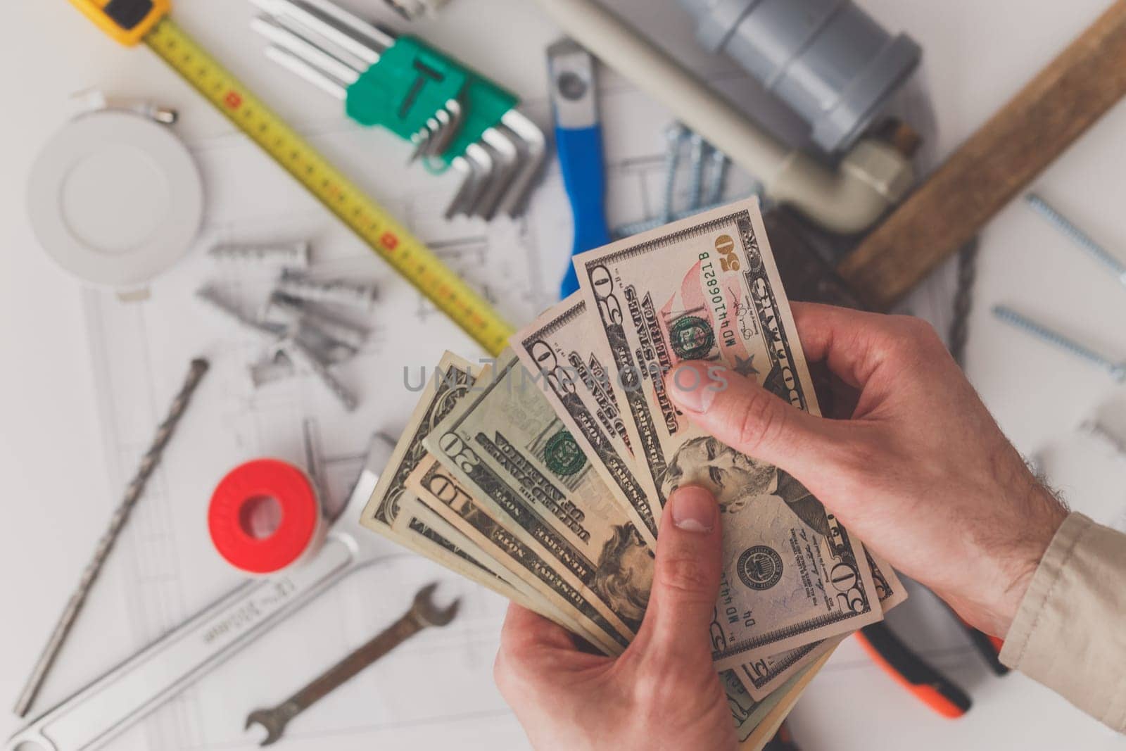 In the foreground men's hands count the costs of repairs or construction. View from above. Building supplies and a drawing in the background.
