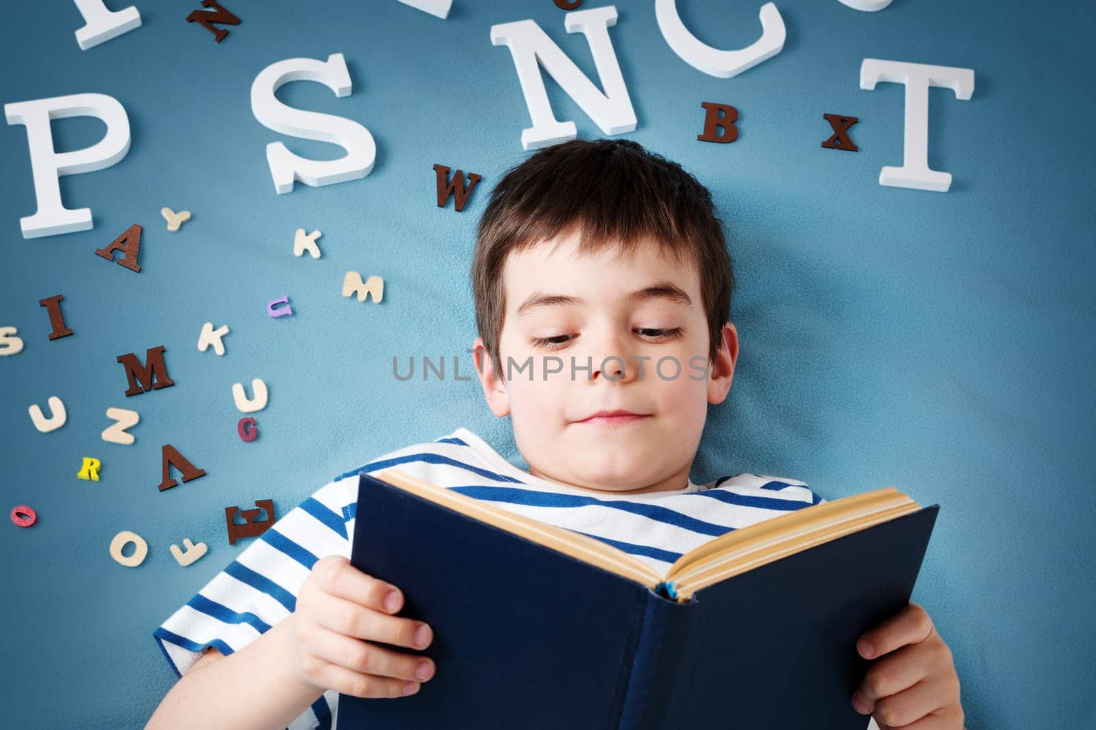 seven years old child lying with book and letters on blue background