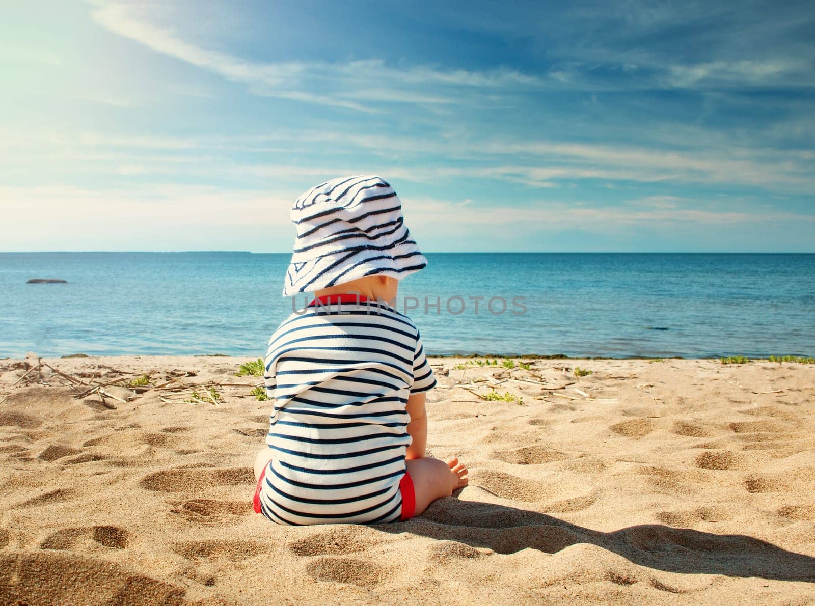 Nine month old baby boy sitting on the beach in beautiful summer day