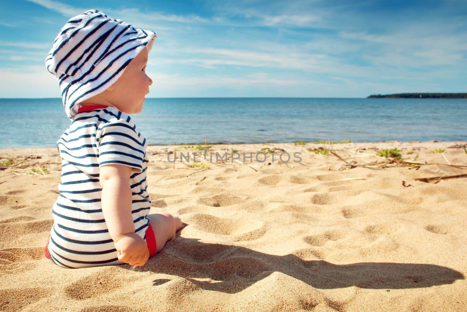 Nine month old baby boy sitting on the beach in beautiful summer day