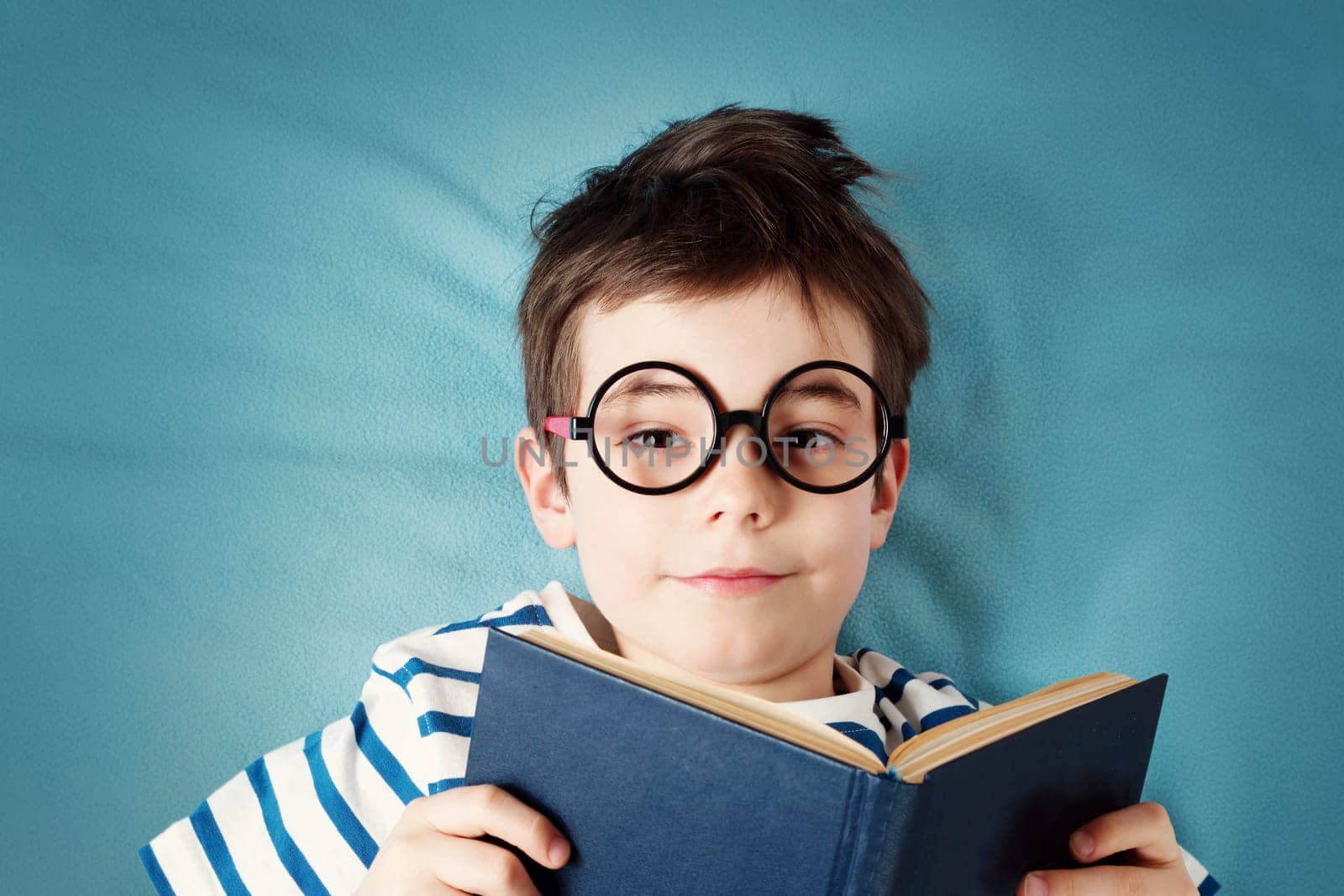 seven years old child lying with book on blue background