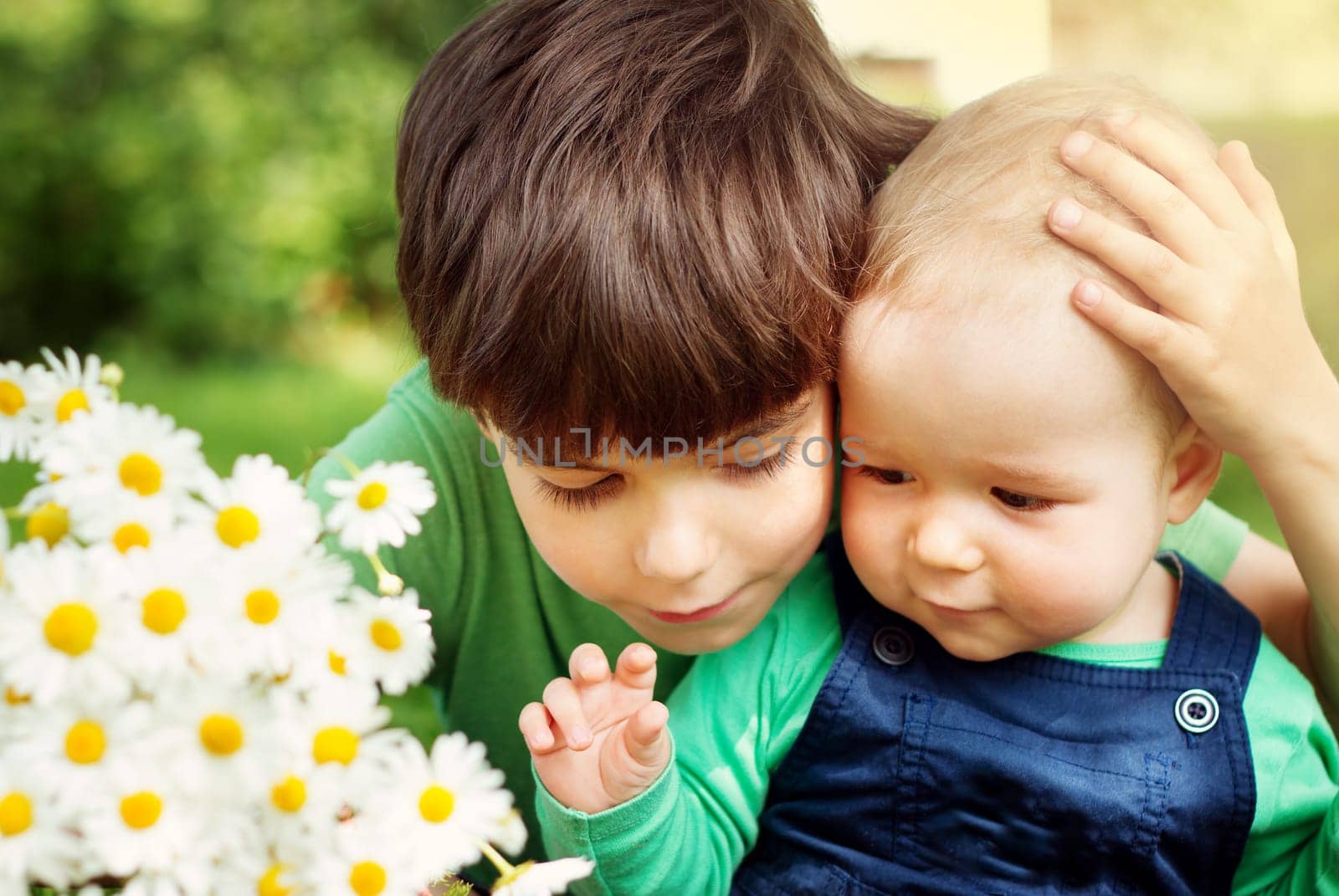 Two lovely brothers sitting in park with flowers hugging