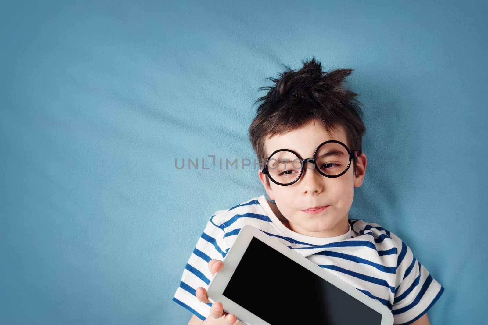 seven years old child lying with tablet on blue background