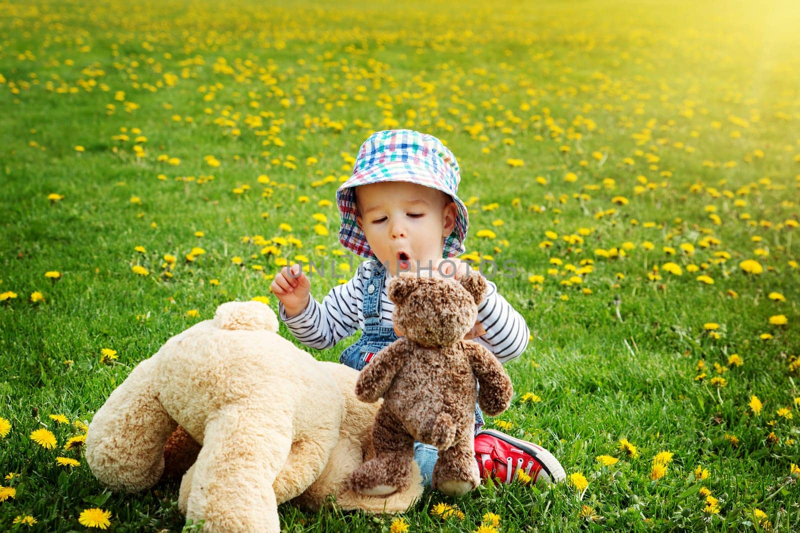 Little boy in hat standing on the field with soft toys in summer