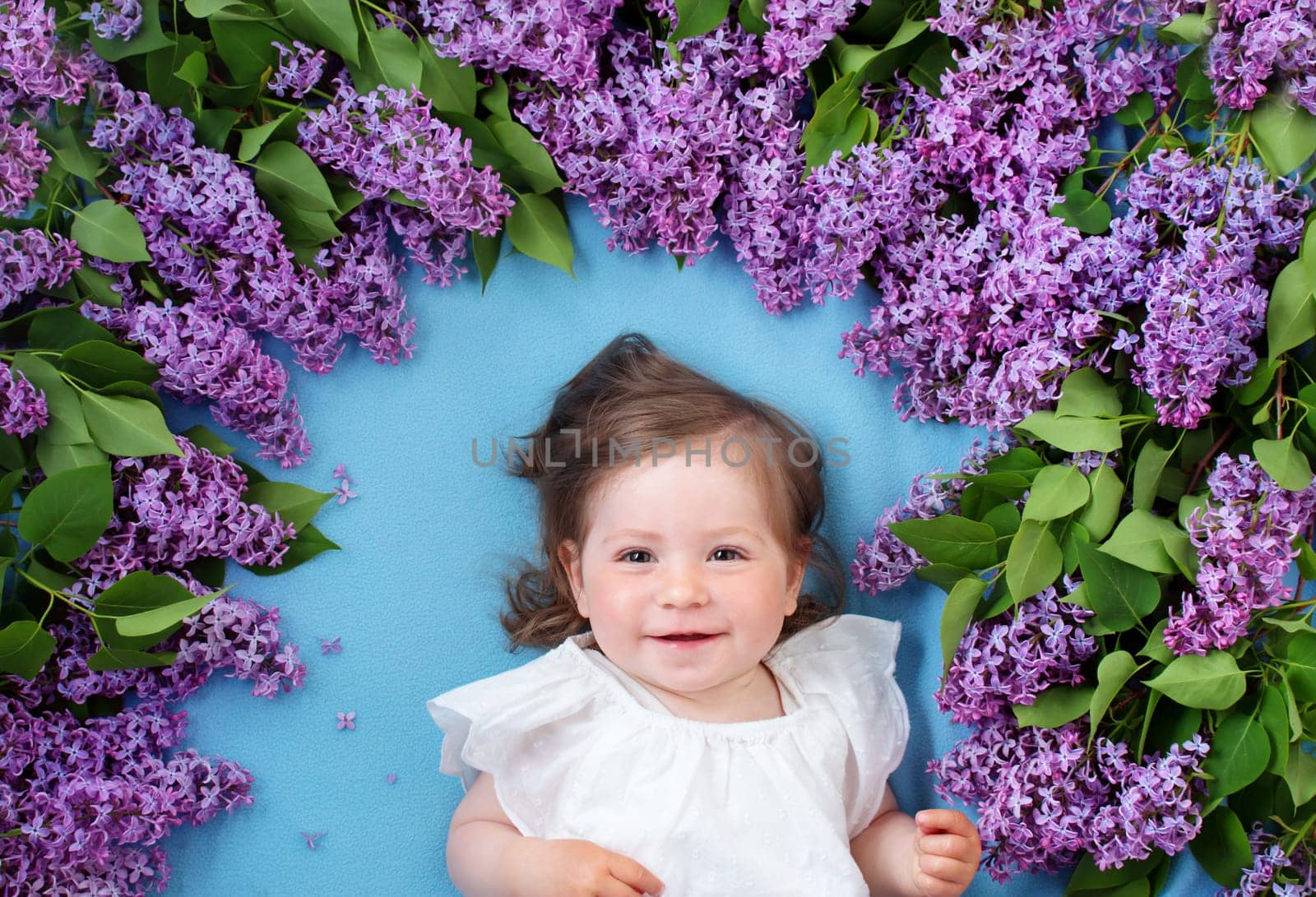 pretty little baby girl lying on blue background with lilac flowers