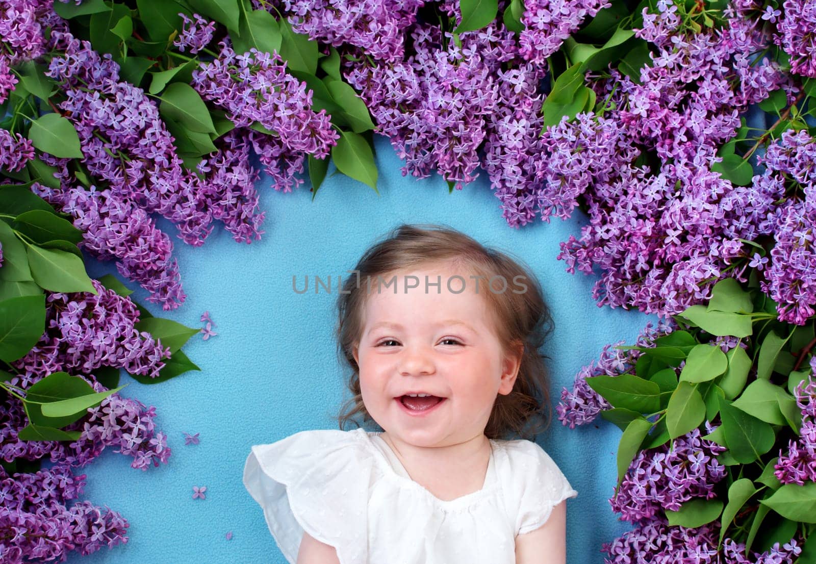pretty little baby girl lying on blue background with lilac flowers