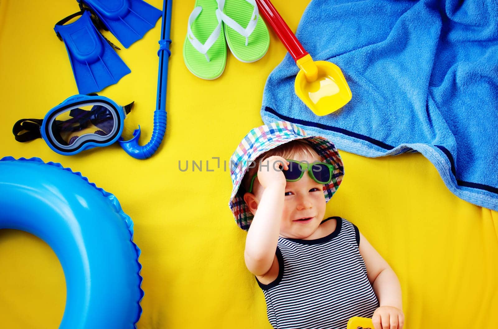 little boy with sunglasses in hat on yellow blanket