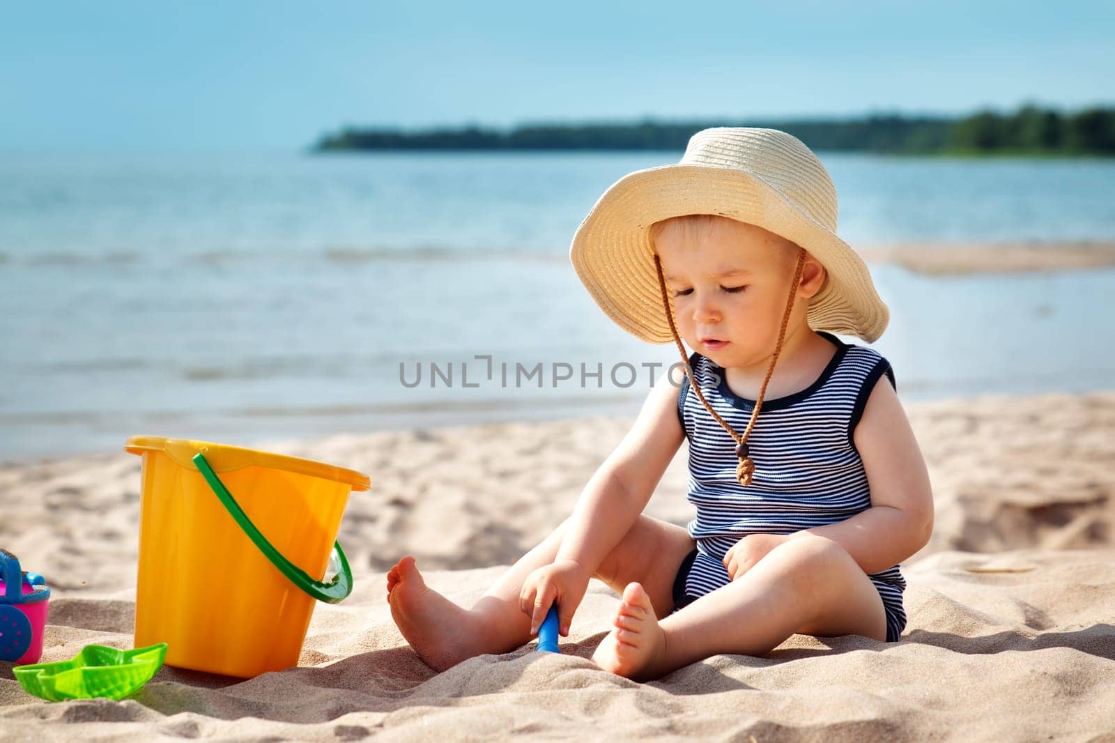 one year old baby boy sitting on the beach in beautiful summer day