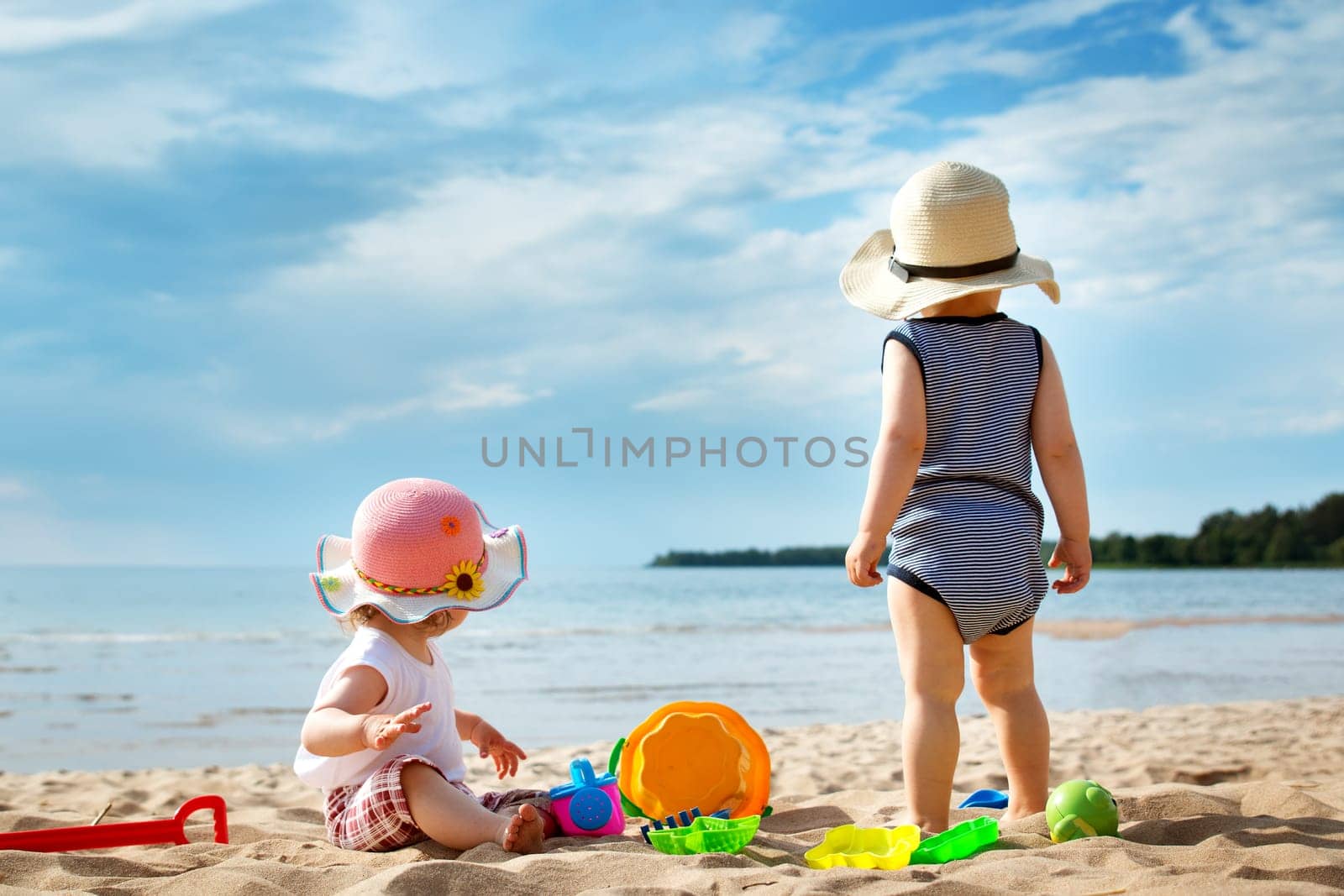 Babygirl and babyboy on the beach in straw hats
