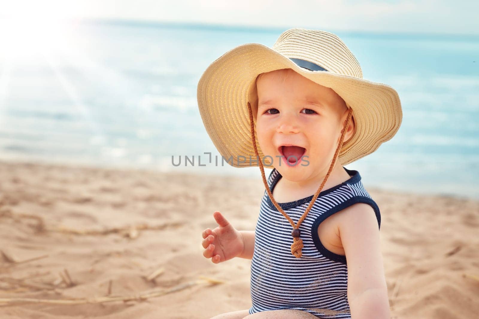 one year old boy sitting at the beach in straw hat