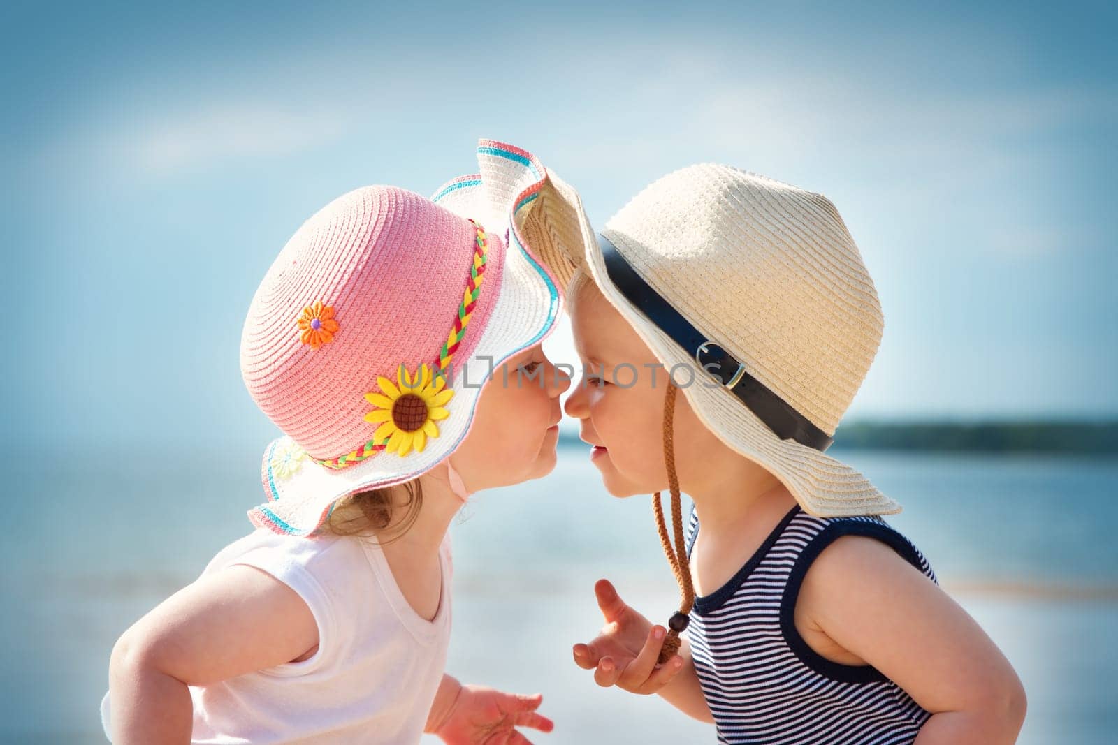 Babygirl and babyboy kissing on the beach in straw hats