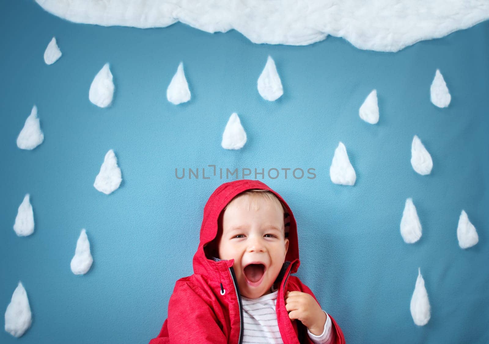 Little boy on blue background in coat with drop shapes and cloud