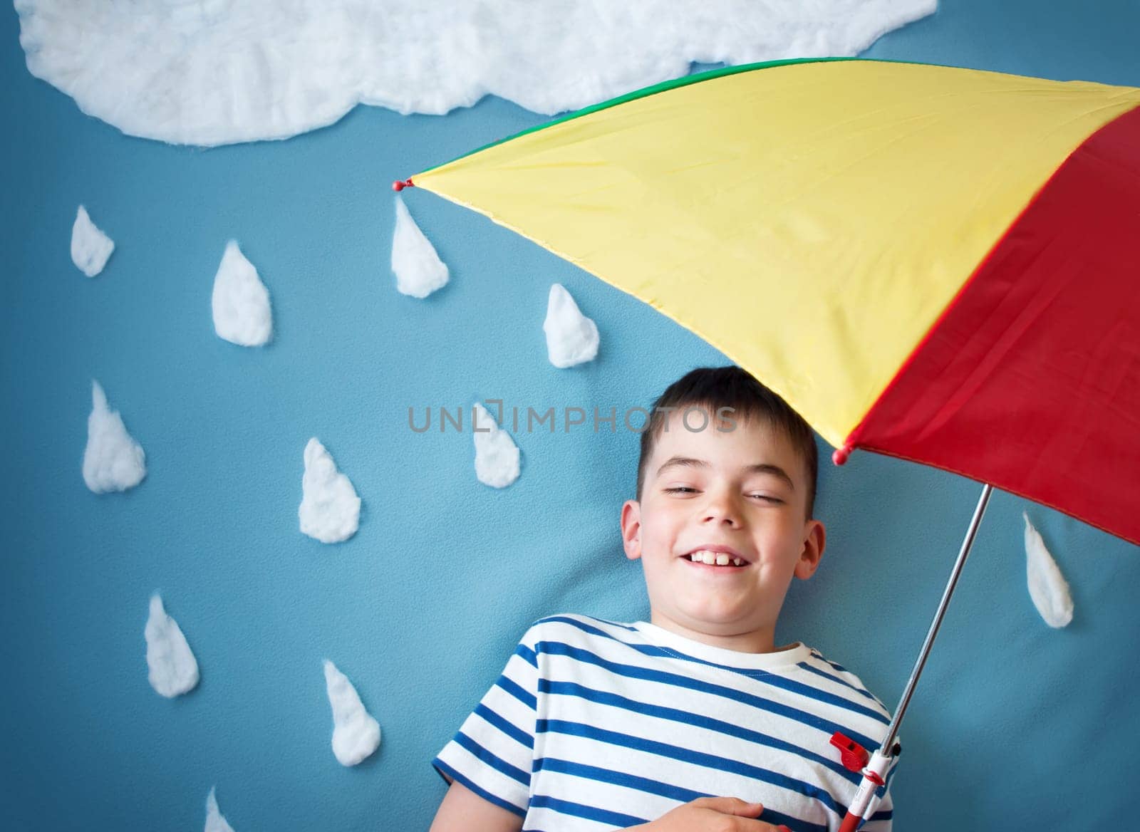 Little boy on blue background in coat with drop shapes and cloud