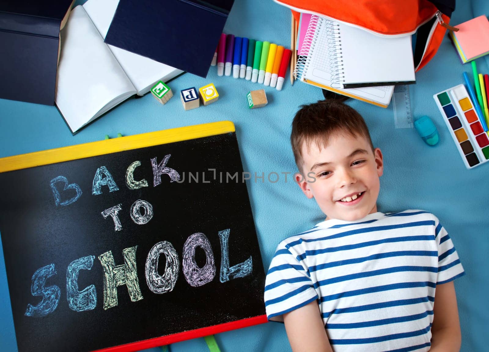 child lying on blue blanket with blackboard and various school accessories