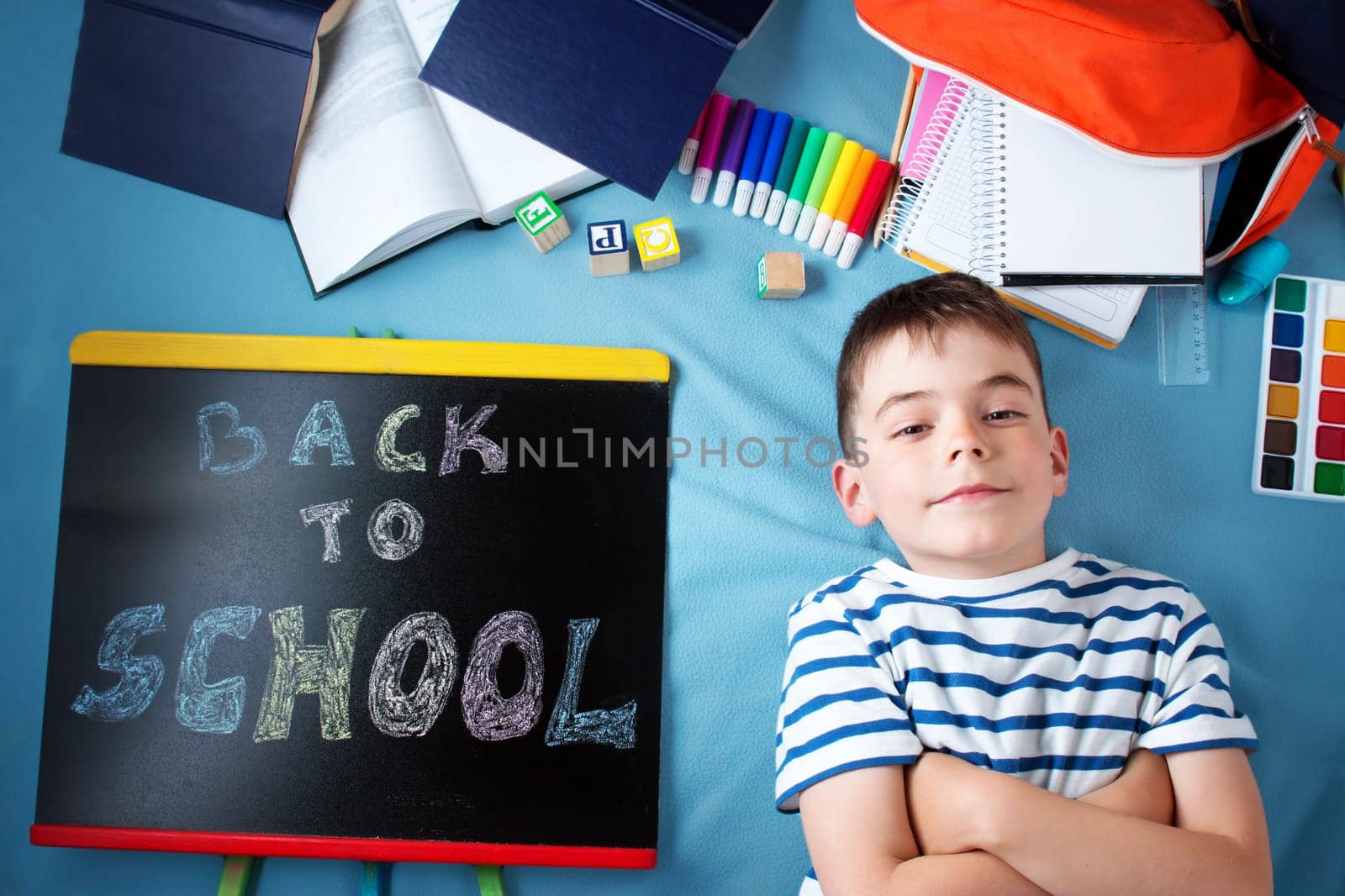 child lying on blue blanket with blackboard and various school accessories