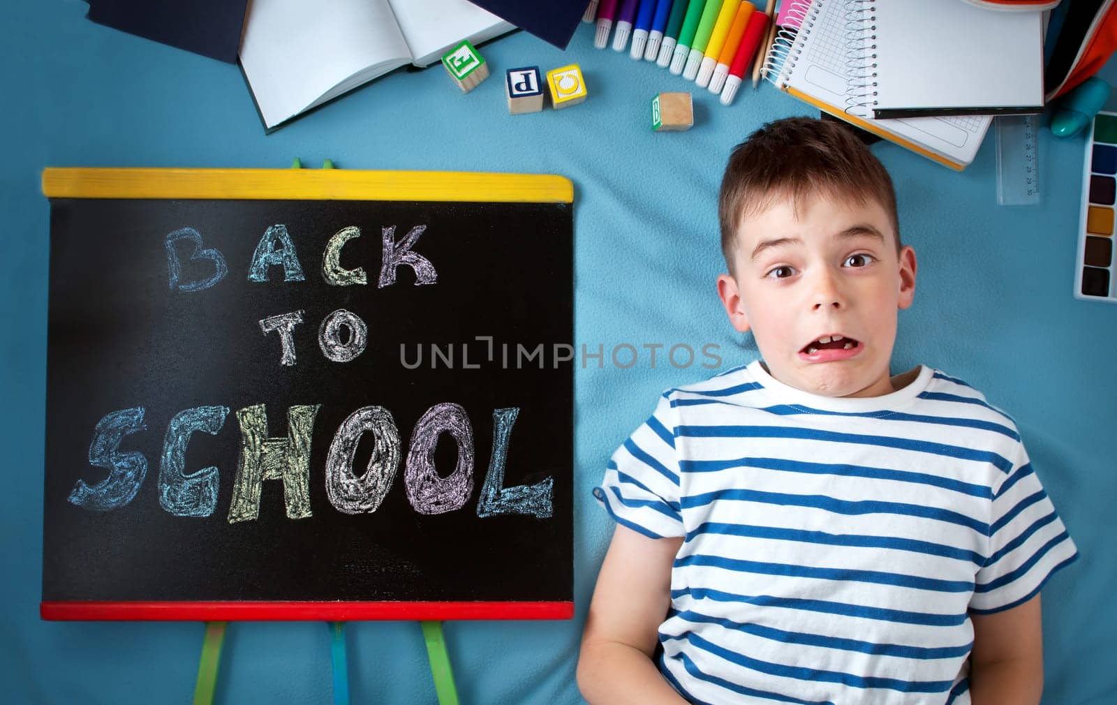 child lying on blue blanket with blackboard and various school accessories