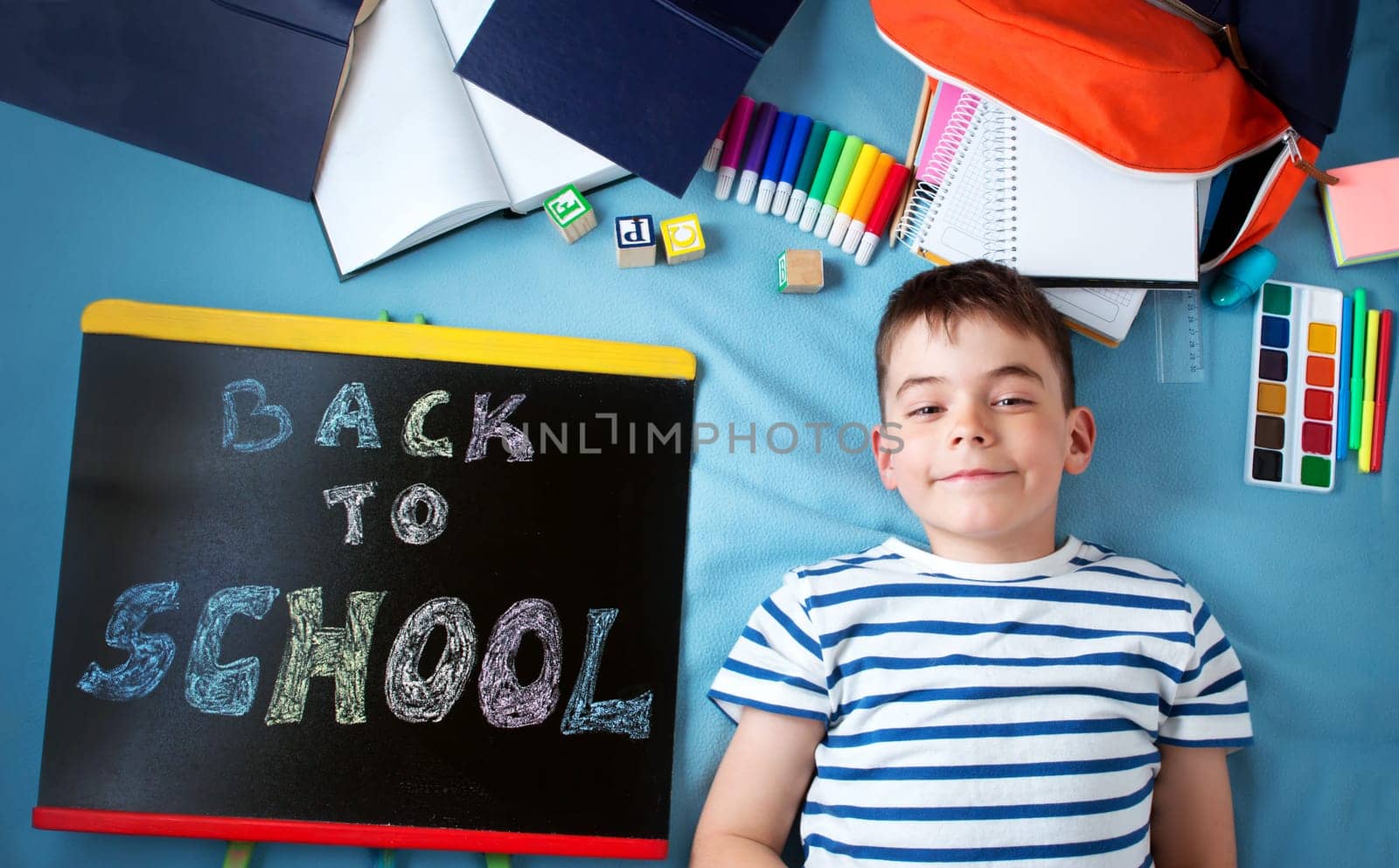 child lying on blue blanket with blackboard and various school accessories