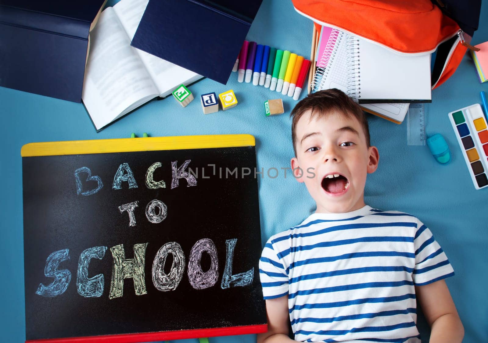 child lying on blue blanket with blackboard and various school accessories