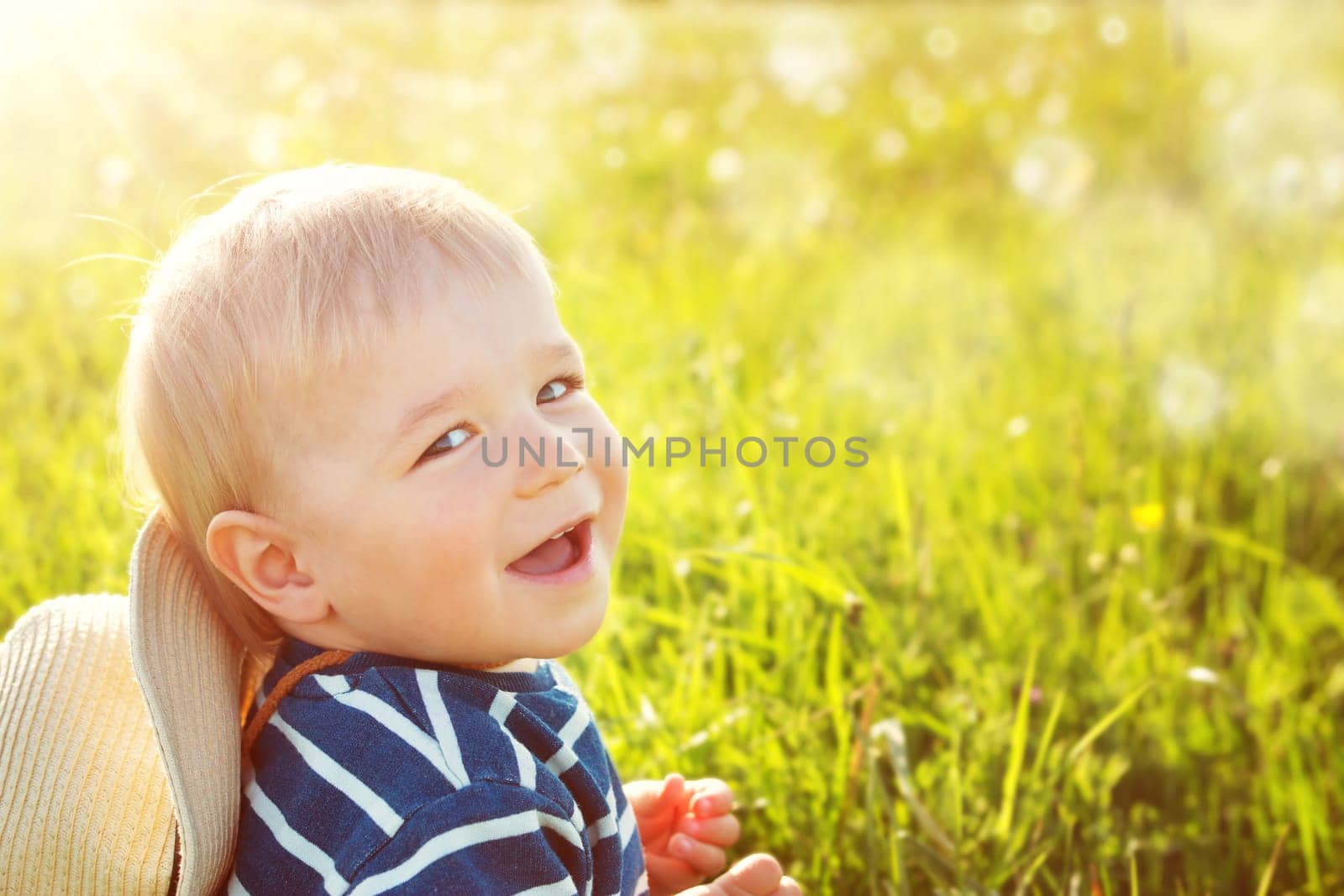 Baby boy sitting in grass on the fieald with dandelions at sunnysummer evening
