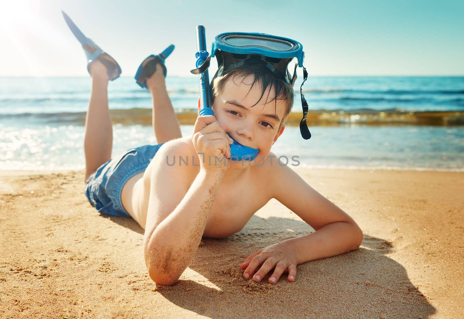Child lying on the beach with swimming mask and flippers. Boy on vacation at sea