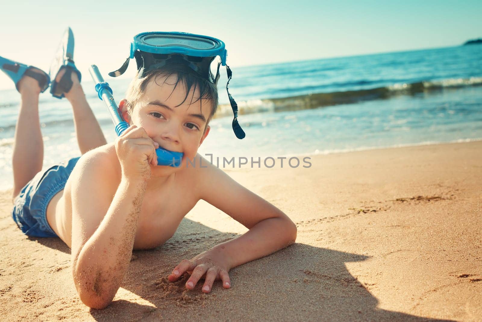 Child lying on the beach with swimming mask and flippers. Boy on vacation at sea