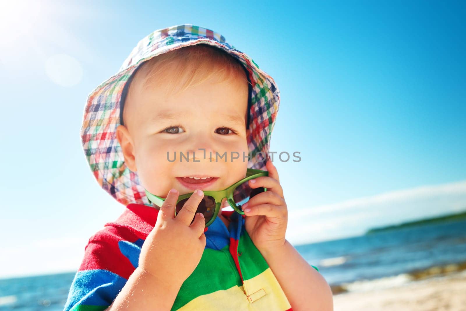 one year old boy smiling at the beach in hat with sunglasses. Child on vacations at sea