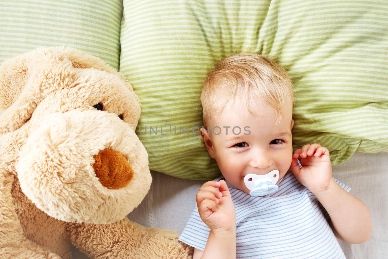 One year old baby lying in the bed with green bedding with soft toy