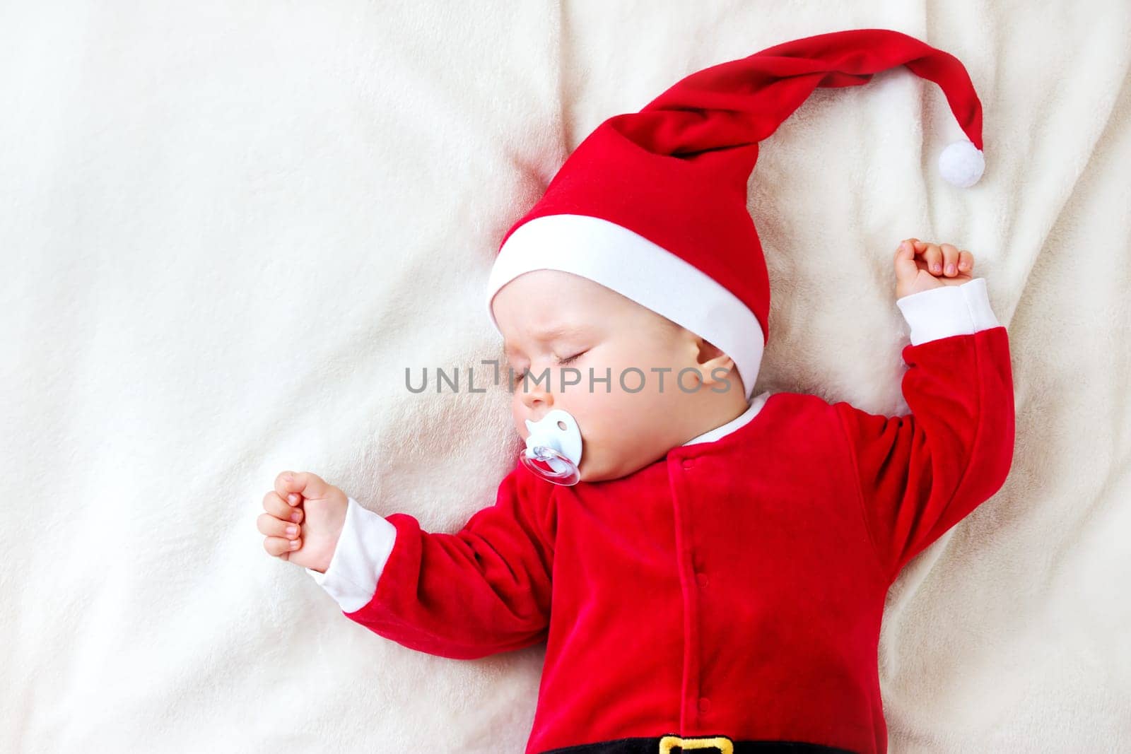 little baby sleeping in red hat on white blanket. Eight month old child in santa costume