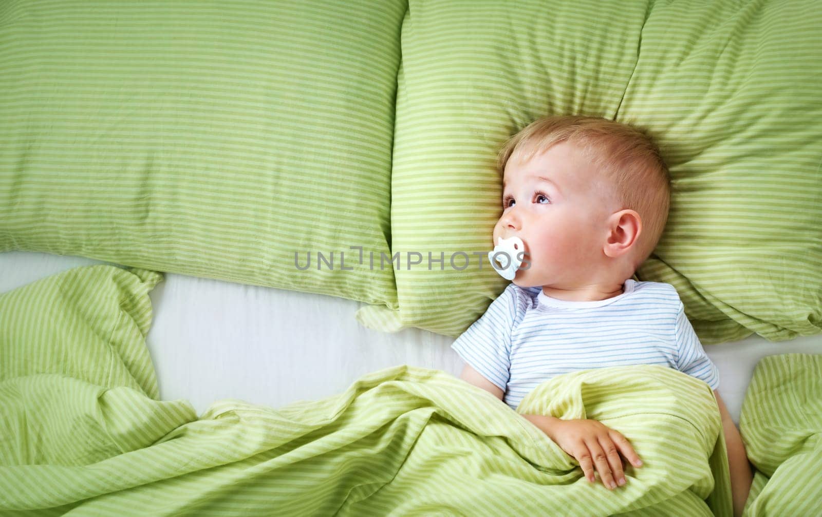 One year old baby lying in the bed with green bedding