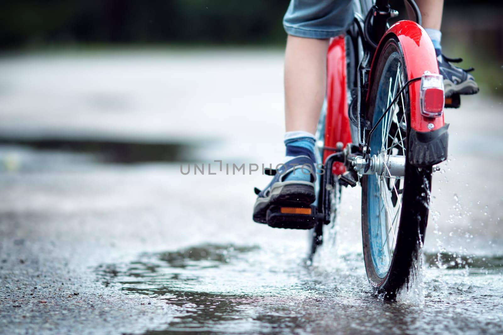 child on a bicycle at asphalt road in summer. Bike in the park moving through puddle on rainy day