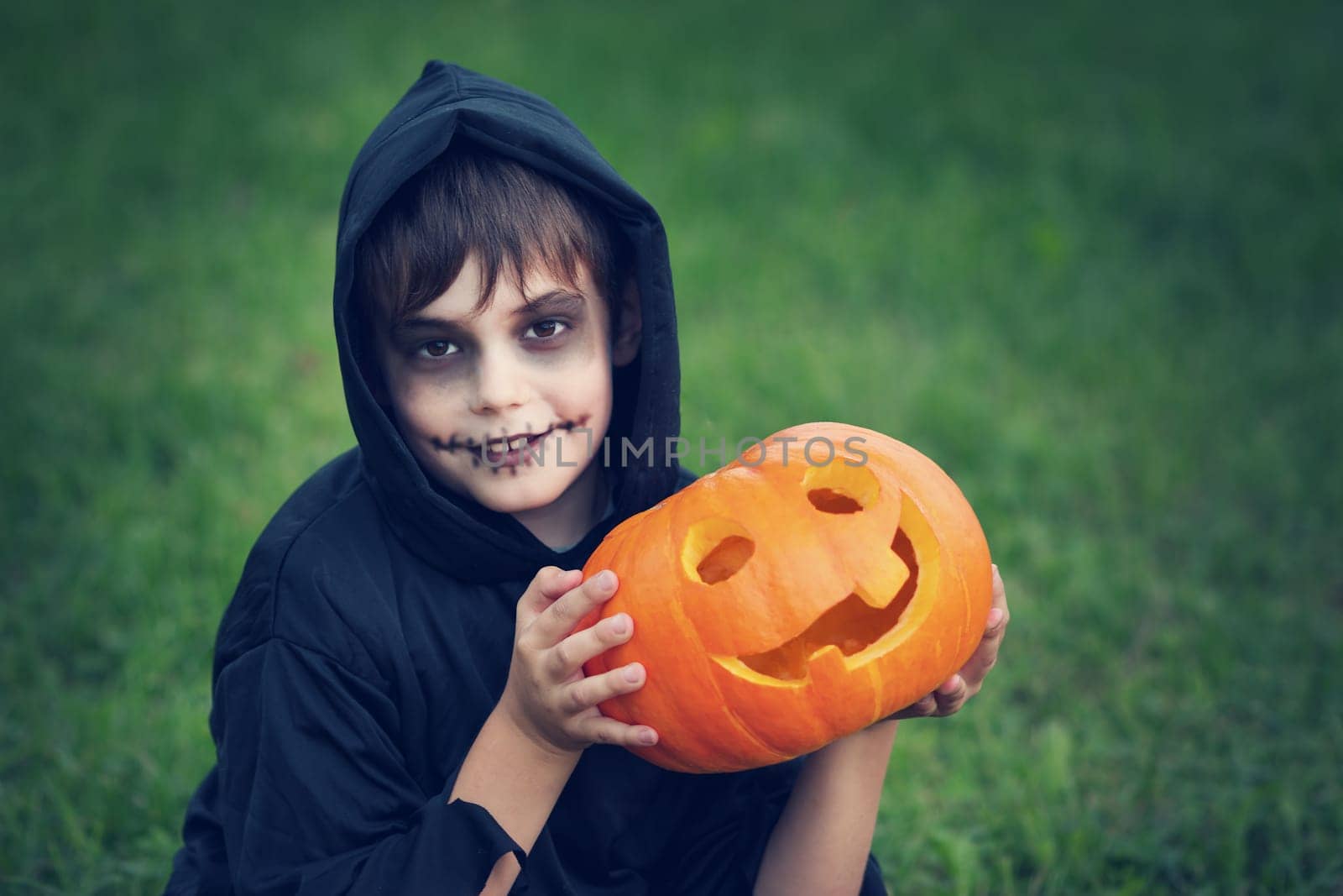 Child in scary costume with pumpkin. Child in halloween outfit playing in the garden