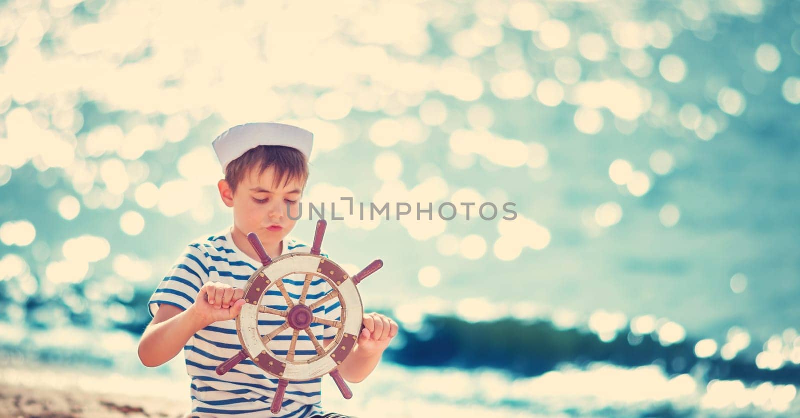 seven years old boy playing at the beach in sailor hat. Child with a steering wheel at sea