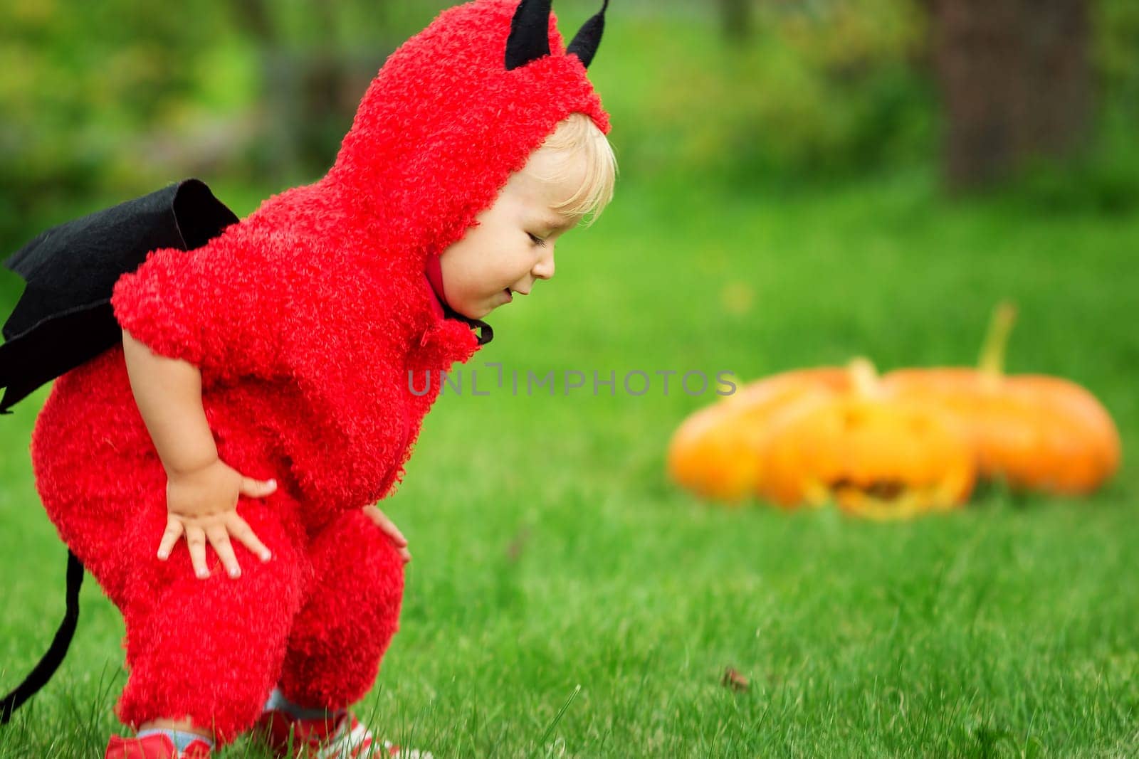 Baby in devil costume with pumpkins. Child in halloween outfit playing in the garden