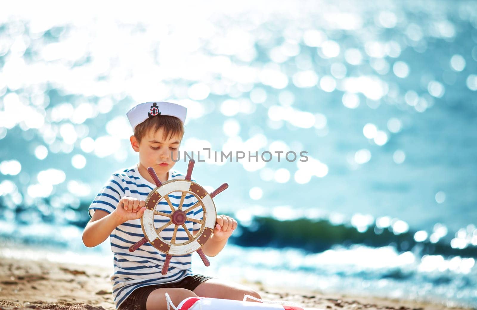 seven years old boy playing at the beach in sailor hat. Child with a steering wheel at sea