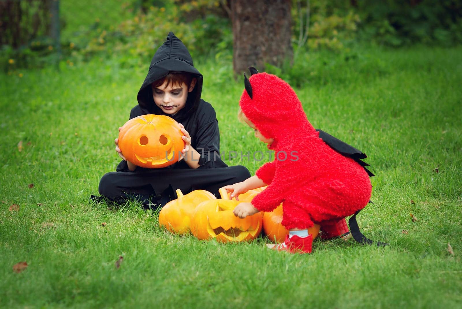 Children in scary costumes with pumpkins. Boys in halloween outfit playing in the garden