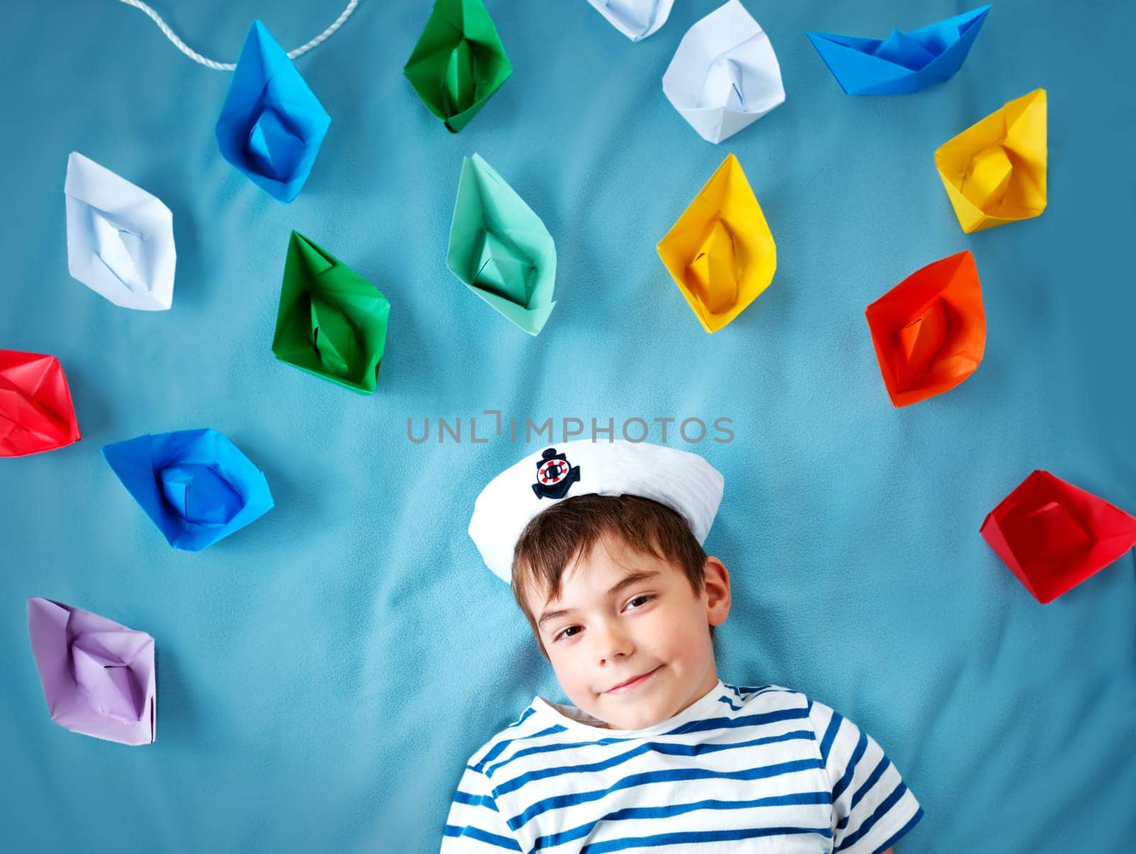 seven years old boy playing in sailor hat. Child withpaper ships on blue background