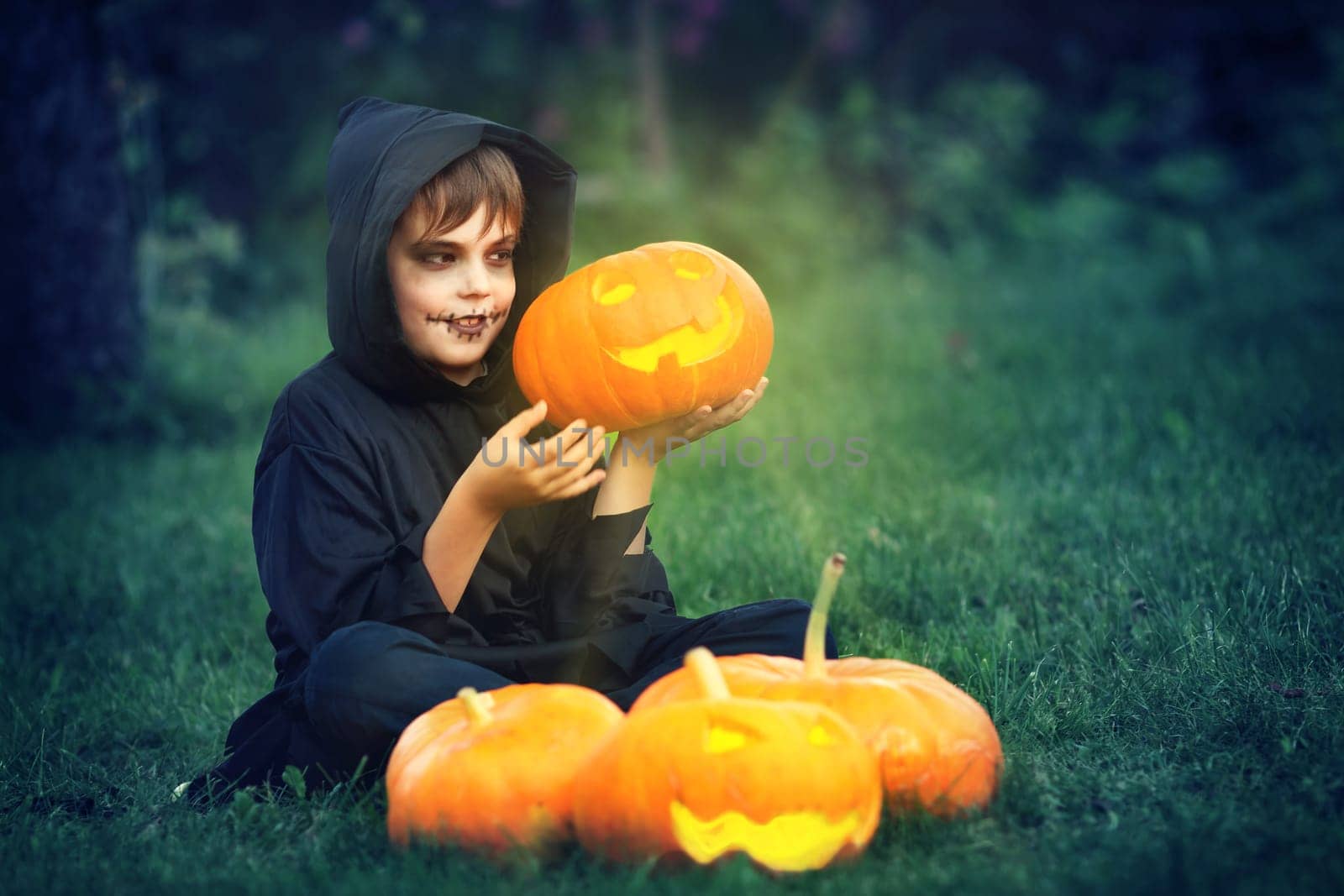 Child in scary costume holding pumpkin ln. Child in halloween outfit at night