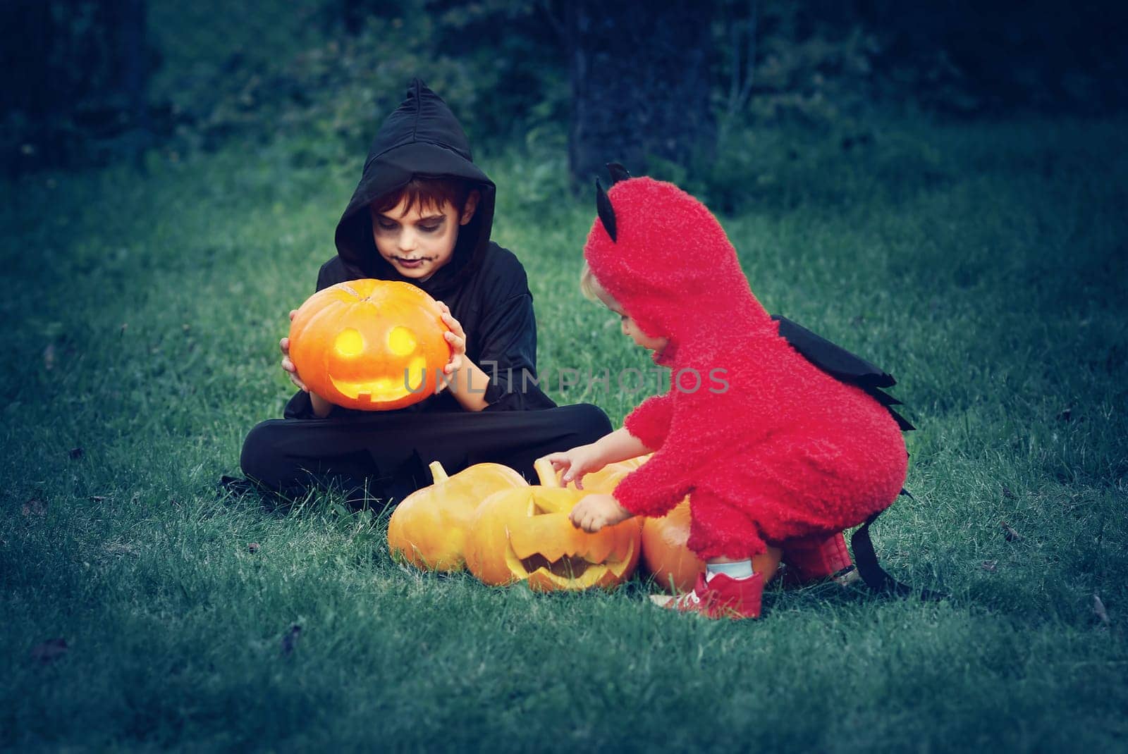 Children in scary costumes with pumpkins. Boys in halloween outfit playing in the garden