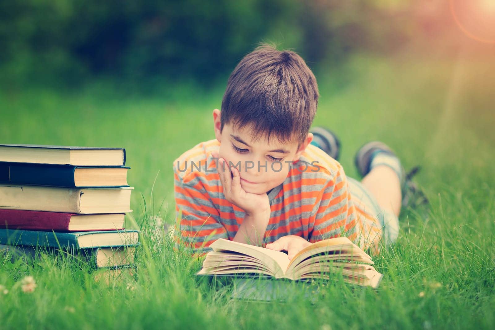 seven years old child reading a book lying on the grass