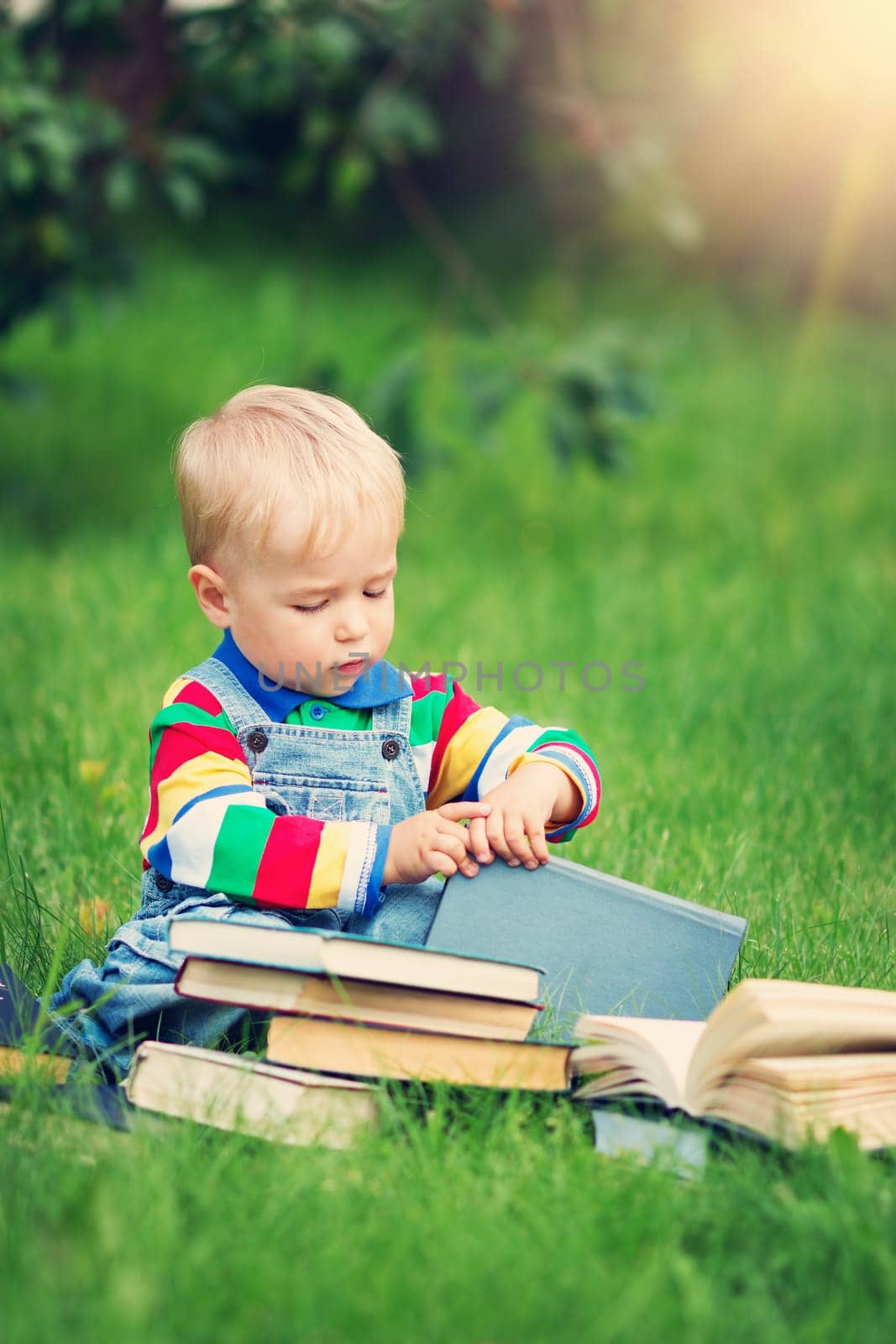one year old baby reading a book sitting on the grass in garden