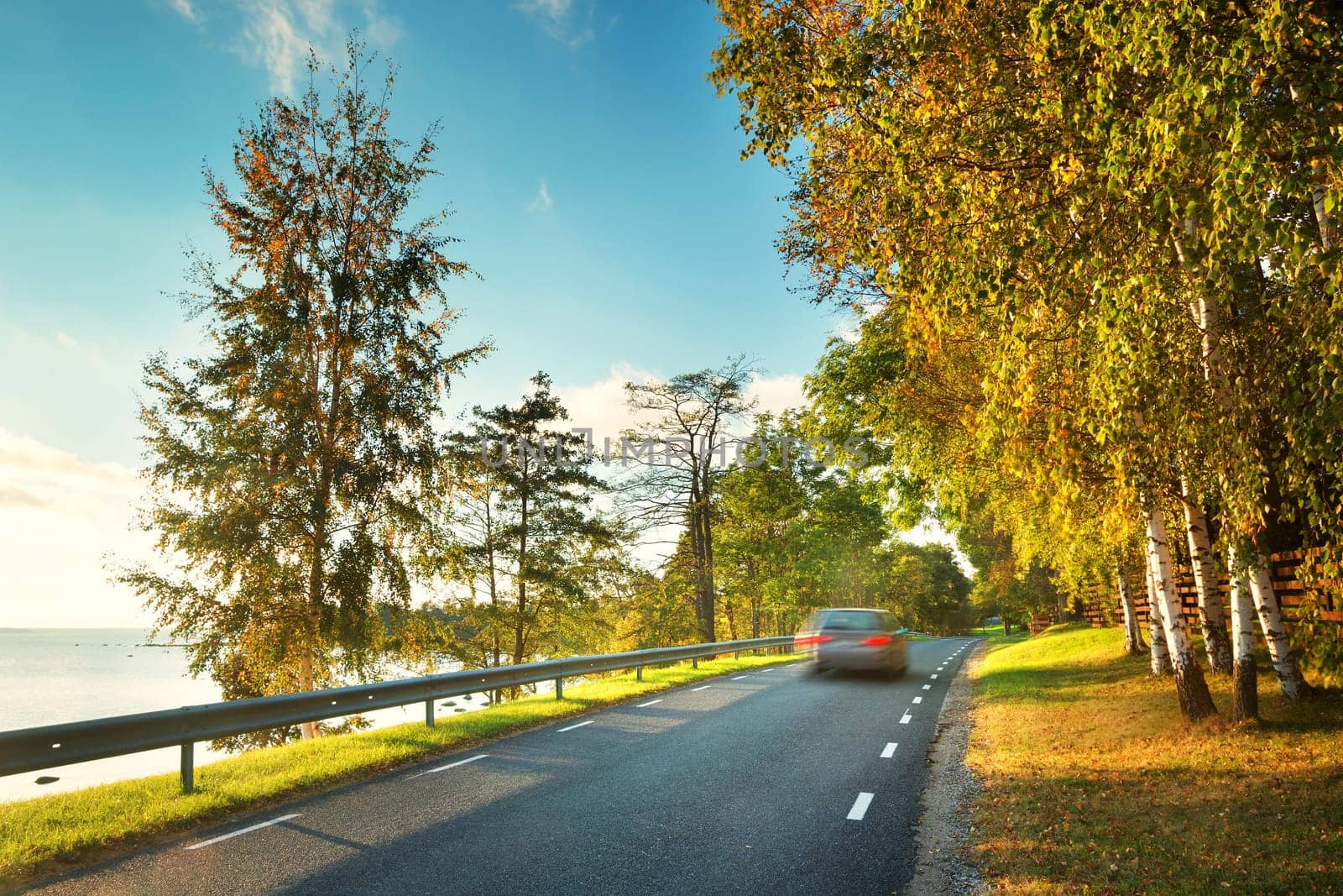 asphalt road with moving car at seaside at sunset