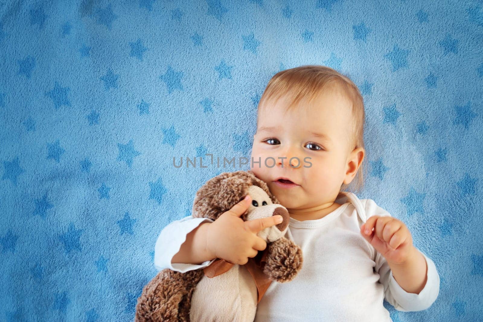 One year old baby lying in bed with a plush teddy bear